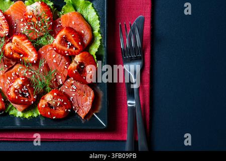 Apéritif de saumon et salade de fraises gastronomique sur une assiette noire, gros plan. Vue de dessus d'un carpaccio de saumon élégant avec des fraises fraîches, des graines de sésame et Banque D'Images