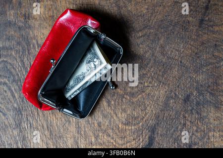 Portefeuille rouge ouvert avec des billets de dollars sur fond en bois, gros plan. Vue de dessus d'un porte-monnaie classique en cuir rouge ouvert contenant de l'argent liquide en dollars américains pliés Banque D'Images