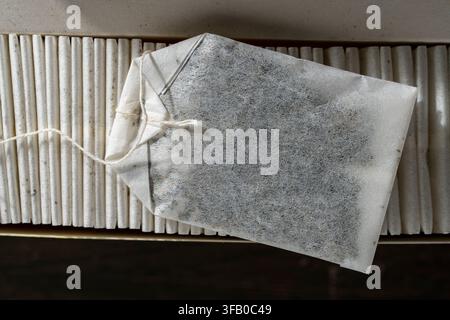 Sac de thé en papier posé au sommet d'une rangée dans une boîte ouverte. Vue de dessus en gros plan d'un seul sachet de thé blanc avec ficelle posé horizontalement sur une rangée soigneusement empilée de sachets de thé en papier Banque D'Images