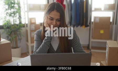 Femme à l'ordinateur portable avec la main sur la joue vérifiant les boîtes d'expédition et les commandes en studio ; planification réfléchie. Banque D'Images