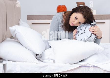 La jeune femme allongée sur le lit dans le concept de gestion du temps Banque D'Images
