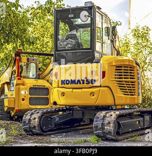 Mini-excavatrice Komatsu jaune garée à l'extérieur sur des chenilles en caoutchouc, entourée d'arbres verts, mettant en valeur des machines de construction compactes dans un chantier Banque D'Images