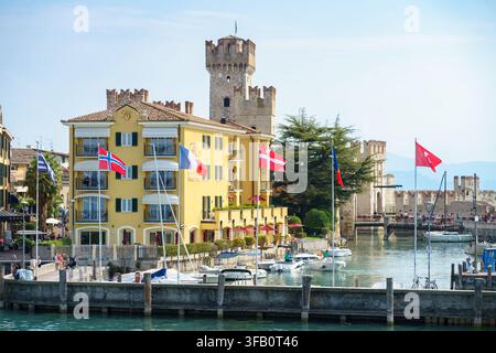 Sirmione, Italie - 27 août 2025 Un château médiéval, un port et des drapeaux internationaux créent une vue emblématique de la ville historique et une atmosphère animée du port de plaisance Banque D'Images