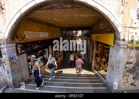 Venise, Italie - 20 juin 2026 : Vue en hauteur encadrée sous une arche de pierre historique érodée, regardant les marches d'escalier vers le bas sur les touristes qui passent Banque D'Images