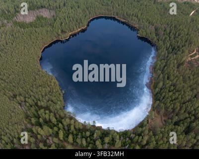 Vue aérienne de dessus d'un lac forestier gelé avec de la glace fissurée en Lettonie Banque D'Images