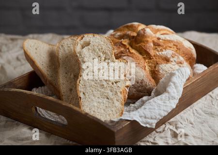 Pain artisanal rustique frais avec des tranches épaisses disposées dans un plateau en bois sur une nappe en lin, mettant en valeur une croûte dorée croustillante et une mie douce faite maison Banque D'Images