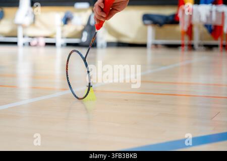 Détail en gros plan d'un joueur de badminton tenant une raquette à côté d'un volant sur un terrain intérieur pendant un tournoi, mettant en évidence l'équipement sportif et m Banque D'Images