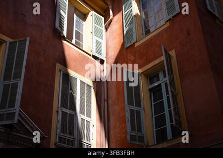 La lumière du soleil illumine les volets pastel et les façades ocre chaudes dans le vieux centre historique de Nice, en France, capturant le charme architectural intime de Banque D'Images