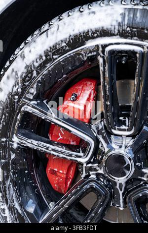 gros plan détaillé d'une jante en alliage noir recouverte de mousse de savon blanche lors d'un lavage extérieur, mettant en évidence la jante brillante, la bande de roulement et la nouvelle pièce brillante Banque D'Images