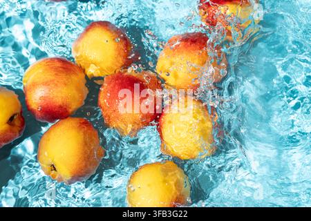 Les nectarines mûres éclaboussent et flottent dans l'eau turquoise claire de la piscine, créant des ondulations et des bulles vibrantes pour une esthétique rafraîchissante estivale colorée Banque D'Images