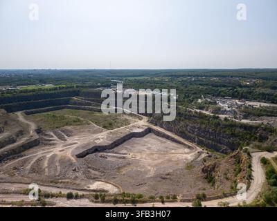 Un plan aérien pris par drone capture une immense carrière de pierre en terrasses avec des champs d'excavation, des routes de terre et des installations de traitement distantes entourées Banque D'Images