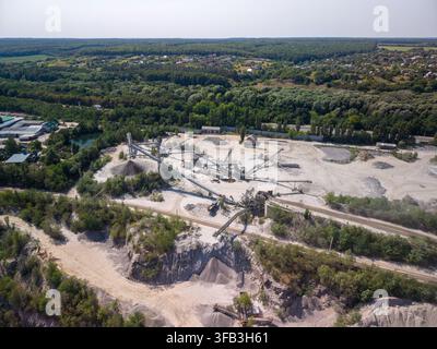 Un large plan aérien par drone capture une installation industrielle de broyage de pierre avec des convoyeurs et des machines de traitement entourés d'arbres verts, de zones de stockage et Banque D'Images