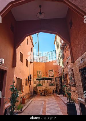 Cour traditionnelle marocaine à Marrakech, Maroc, avec des murs en terre cuite, des carreaux décoratifs, une architecture en arc, des plantes et des sièges extérieurs Banque D'Images