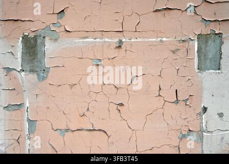 Vue horizontale d'une surface murale peinte en brun clair usée avec de la peinture craquelée et écaillée, deux taches rectangulaires en béton, zone peinte en gris clair Banque D'Images