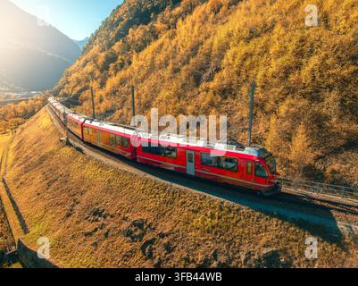 Vue aérienne du train rouge dans les montagnes alpines avec des prairies verdoyantes Banque D'Images