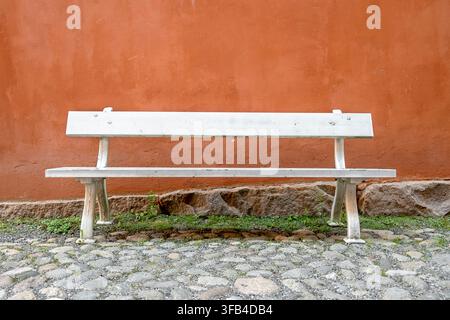 Banc en bois blanc vide contre un mur en béton orange, siège extérieur abandonné Banque D'Images