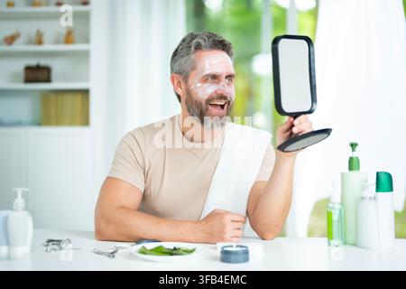 La routine de beauté matinale utilise des cosmétiques pour le visage. Les soins matinaux hydratent la peau d'âge moyen. Un homme mûr applique une crème pour le visage le matin. Spa à domicile Banque D'Images