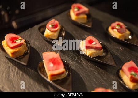 Une vue en hauteur d'appetizers de thon ahi sautés gourmet servis sur de petits carrés de pain grillés dans des cuillères à dégustation noires, magnifiquement disposés sur un fond sombre Banque D'Images