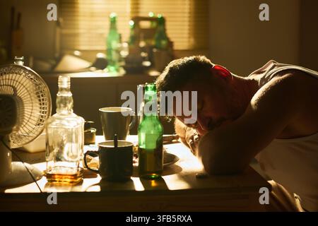 Homme déprimé dormant sur la table de la cuisine avec des bouteilles d'alcool Banque D'Images