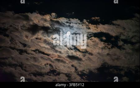 Lune pleine brillante illuminant un ciel nocturne dramatique rempli de nuages texturés, créant un paysage céleste mystérieux et atmosphérique. Banque D'Images