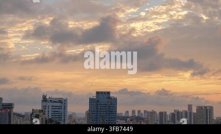 Une ligne d'horizon urbaine au coucher du soleil, avec des immeubles résidentiels en hauteur s'élevant au-dessus d'un mélange de tours modernes et de maisons basses aux toits rouges Banque D'Images