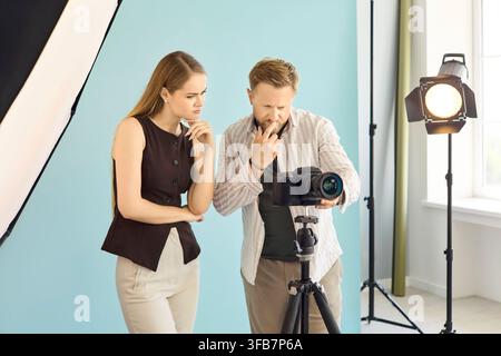 Photographe et modèle examinant l'appareil photo sur trépied dans le studio avec éclairage Banque D'Images