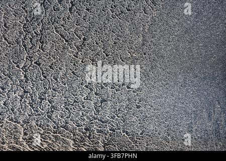 Une surface d'asphalte texturée avec des motifs de poussière complexes et des tons gris érodés créant un fond industriel abstrait pour le design Banque D'Images