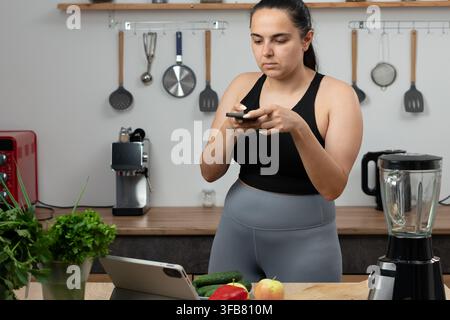 Blogueuse fitness prenant une photo de nourriture saine en cuisinant une salade dans la cuisine. Concept de blogue sur la nourriture, la nutrition et la perte de poids Banque D'Images