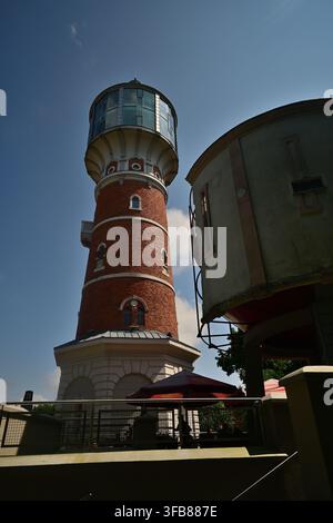 Un château d'eau historique en briques rouges transformé en tour d'observation contre un ciel bleu clair avec une terrasse de café en plein air en dessous - la ville de Masurie Banque D'Images