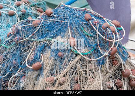 Un tas enchevêtré de filets de pêche bleus et blancs avec des flotteurs repose sur le pont d'un bateau. Banque D'Images