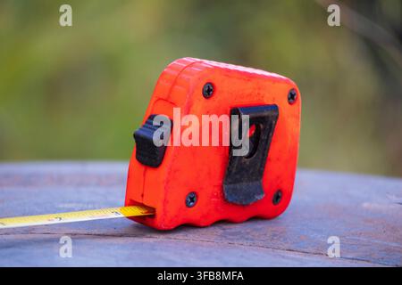 Grossissement d'un mètre ruban orange avec une lame jaune reposant sur une surface métallique rustique en plein air Banque D'Images