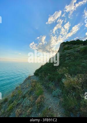 Falaise côtière rocheuse surplombant une mer bleue calme sous des nuages lumineux du soir Banque D'Images