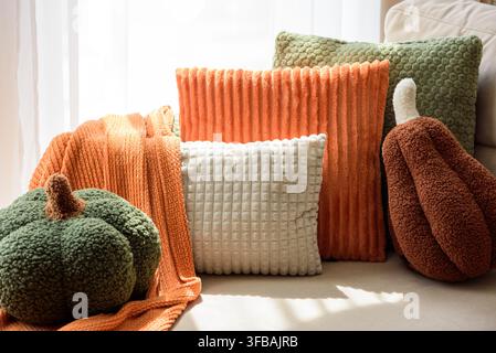 Des citrouilles en textile doux et moelleux de tailles variées et de couleurs terreuses sont disposées avec art avec des coussins accentués en maille nervurée et gaufrée. Une lumière chaude et ambiante Banque D'Images