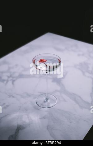 Un cocktail élégant et cristallin dans un verre à martini, délicatement garni d'une fleur de cerisier flottante, posé sur une table en marbre blanc Banque D'Images