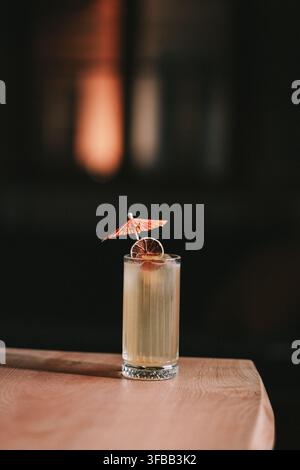 Cocktail Tiki avec un parapluie en papier et un citron vert séché dans un grand verre sur une table en bois dans un bar sombre Banque D'Images