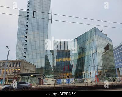 Bâtiments de bureaux modernes angulaires en verre avec des façades réfléchissantes dominant une scène de rue urbaine. Un gratte-ciel élevé avec une façade verticale étagée s'élève Banque D'Images
