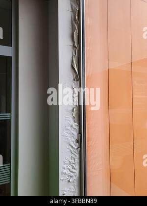 Vue rapprochée de la détérioration de la façade d'un bâtiment montrant une forte décollement de peinture et des dommages causés par l'eau sur un rebord structurel horizontal sous une teinte orange Banque D'Images