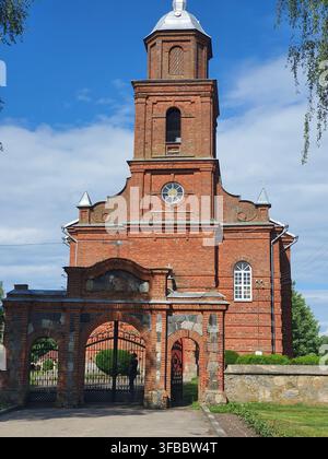 Une église traditionnelle en briques rouges avec un clocher attenant surmonté d'un dôme en métal argenté, présentant une maçonnerie décorative, des fenêtres en arc et une Banque D'Images