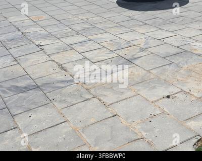Une vue rapprochée d'une surface pavée extérieure présentant des carreaux rectangulaires en pierre ou en béton gris disposés selon un motif en damier décalé. La Banque D'Images