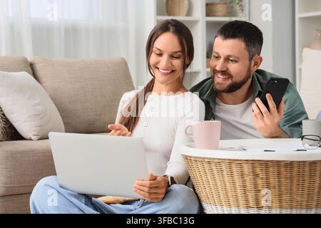 Travail à distance et style de vie numérique, couple heureux utilisant un ordinateur portable et un smartphone à la maison, communication en ligne et vie moderne Banque D'Images