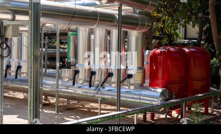 Système industriel de chauffage et de circulation d'eau avec des tuyaux en acier inoxydable, des composants cylindriques et des réservoirs de pression rouges installés à l'extérieur dans une installation Banque D'Images