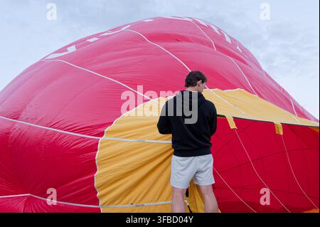 Membre d'équipage inspectant la bouche d'un ballon à air chaud partiellement gonflé à froid. Banque D'Images