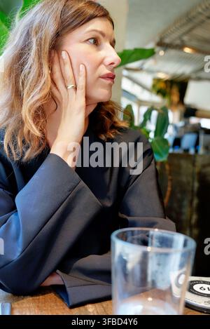 Femme reposant sa main sur sa joue à une table de café Banque D'Images