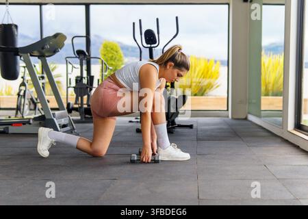 Femme effectuant un exercice de fente avec des haltères dans une salle de sport moderne et lumineuse Banque D'Images