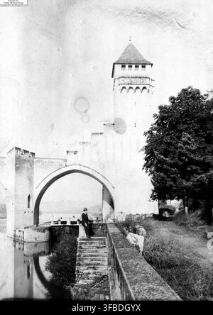 Le Pont Valentré, un pont en pierre médiéval avec une tour à Cahors, Midi-Pyrénées, France, photographié avec des femmes à proximité, parmi des arbres et des escaliers menant à une zone voûtée. Banque D'Images