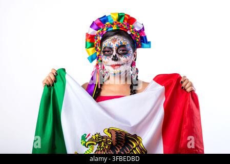 Femme souriante avec un maquillage du Jour des Morts tenant le drapeau mexicain sur fond blanc. Banque D'Images