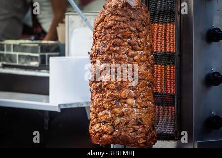 Grossissement d'une viande de kebab assaisonnée grillant sur un brochette verticale à côté d'un brûleur à gaz, montrant le rôti en couches utilisé pour les döner et shawarma dans la nourriture de rue Banque D'Images