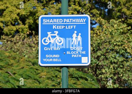 Panneau de chemin partagé bleu avec des règles pour les cyclistes et les piétons, sur un fond vert feuillu en Australie Banque D'Images