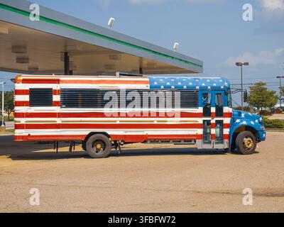 Un bus scolaire personnalisé peint avec le drapeau américain garé à une station-service sous un ciel bleu clair Banque D'Images