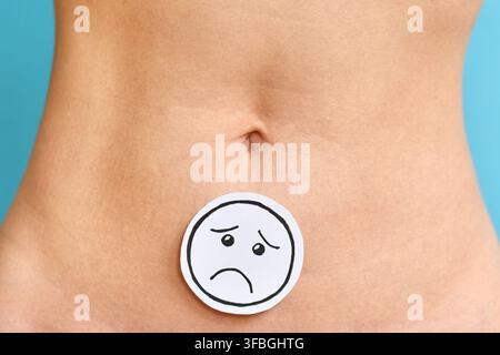 Visage triste sur l'abdomen d'une femme symbolisant les douleurs menstruelles, l'endométriose, les problèmes de fertilité et les problèmes de santé reproductive Banque D'Images